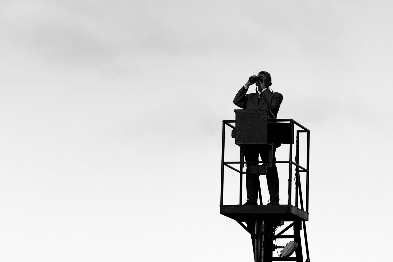 About Elsewhere text on black and white photo of man on a elevated platform looking through binoculars.